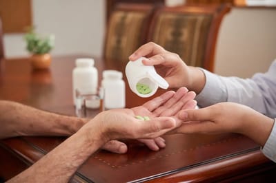 Hands exchanging medication in a care setting.