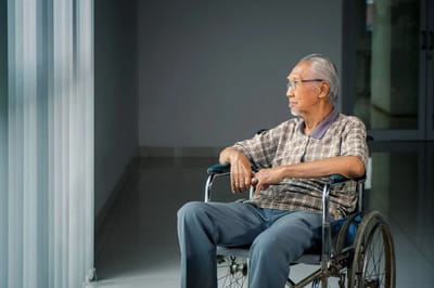 Elderly man in a wheelchair looking out a window.