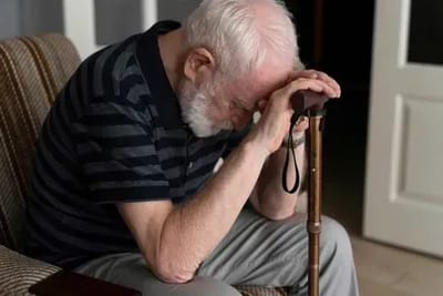 Elderly man resting with his head down on a cane