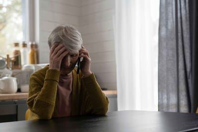 Elderly woman on the phone looking distressed.