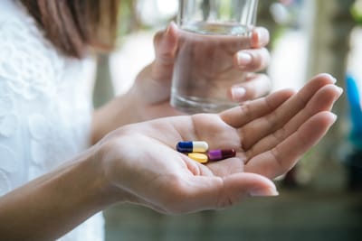 Person holding pills and a glass of water.