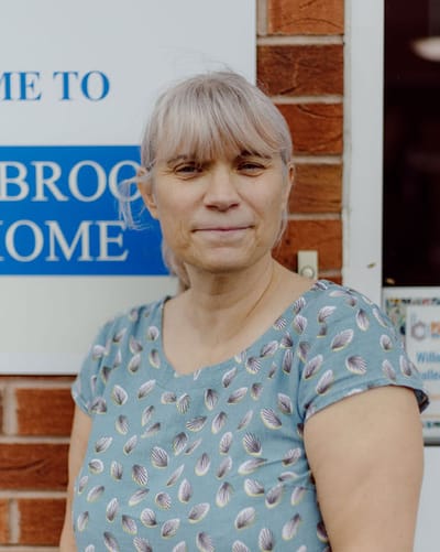 Woman smiling in front of Willowbrook Care Home sign.