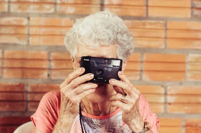 Elderly woman holding a camera, smiling.