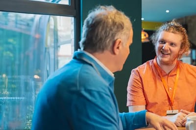 Two men engaged in conversation inside a common area.