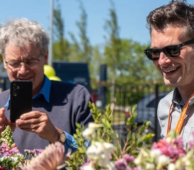 Two men enjoying flowers outdoors at a facility event.