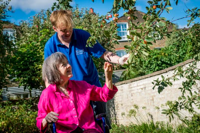 A resident picking fruits with staff in the garden.