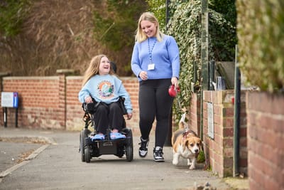 Young girl in wheelchair with caregiver and dog outdoors