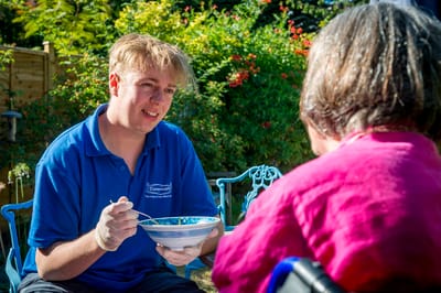 Staff member feeding a resident outdoors.