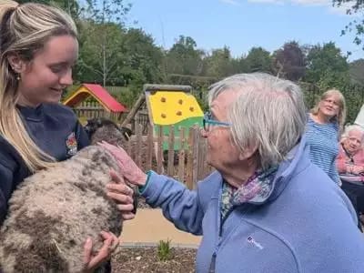 Resident interacting with staff and petting a sheep.