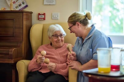 Senior resident engaging in a musical activity with staff.