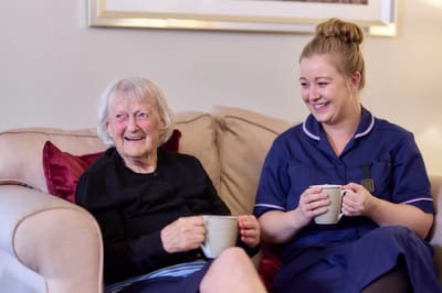Resident and caregiver smiling while sitting together.
