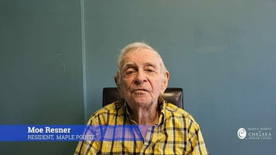 Resident sitting in a chair with a blue wall behind.