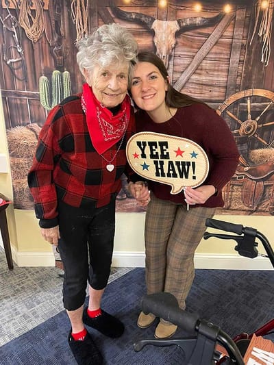 A resident and staff member smiling together with a fun prop