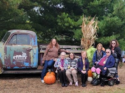 Residents posing outdoors with pumpkins and a vintage truck