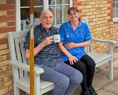 A resident enjoying tea with staff in a garden area