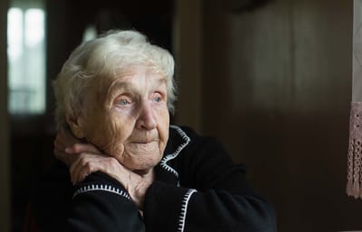 An elderly woman looking thoughtfully out a window
