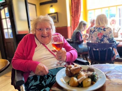 Resident enjoying a meal with a drink in a warm setting