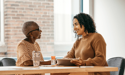 Two women talking at a table in an indoor space.