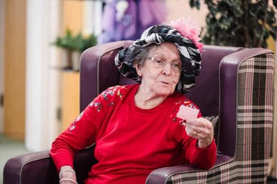 Elderly woman in a colorful hat, reading a card.