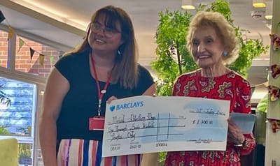 Celebration event with a resident and staff member presenting a check.