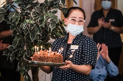 Staff member presenting a birthday cake with candles.