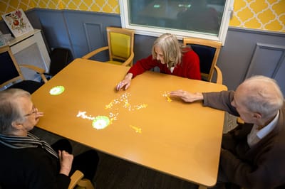 Three seniors engaging with interactive projection on a table.