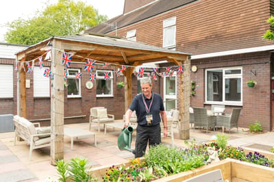 Staff member watering flowers in outdoor garden.