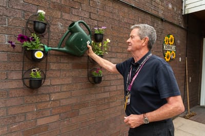 Resident watering plants on a brick wall.