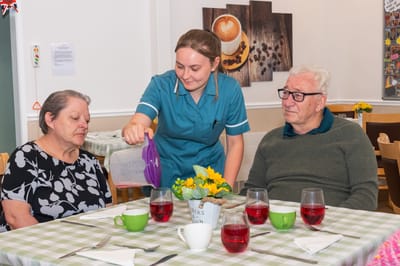 Staff serving drinks to residents at a dining table.