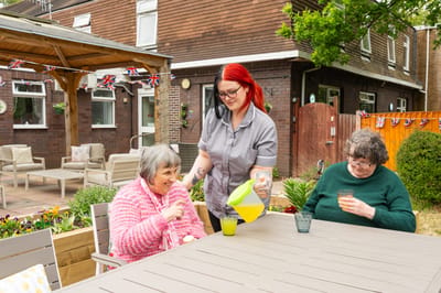 Staff serving drinks to two residents outdoors.