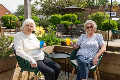 Two elderly women enjoying drinks outdoors in a garden