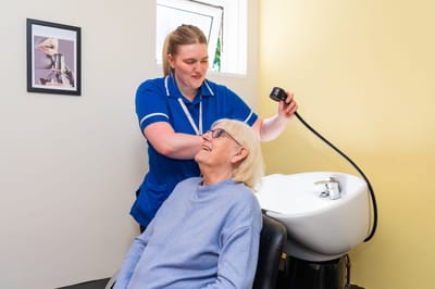 Hair salon scene with a resident receiving a wash.