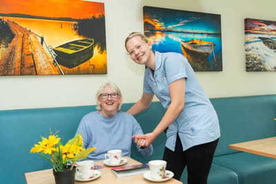 Staff assisting a smiling resident in a common area.