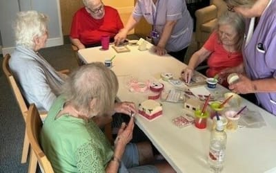 Residents engaged in a craft activity with staff assistance.