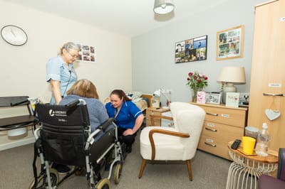 Staff assisting a resident in a cozy room.