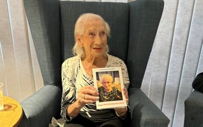 Elderly woman holding a framed photo, smiling.