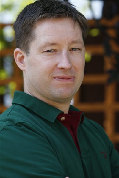 Man standing outdoors, smiling confidently.