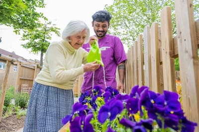 Elderly woman watering flowers with staff support