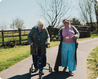 Staff assisting resident outdoors with a walker.