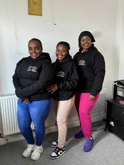 Three staff members in branded hoodies smiling together.