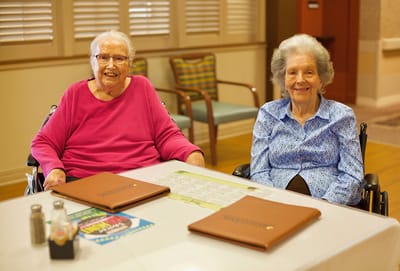Two elderly women seated at a dining table.