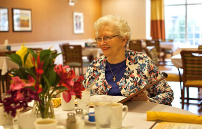 Elderly woman at a dining table in a shared space.