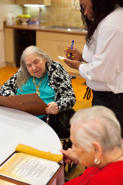 Residents interacting with staff in a dining area.