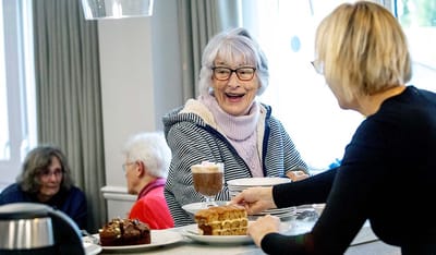 Resident enjoying food with staff assistance.