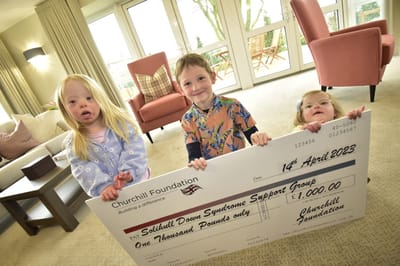 Children holding a large charity check in a common area