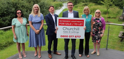 Group of people holding a 'For Sale' sign outdoors