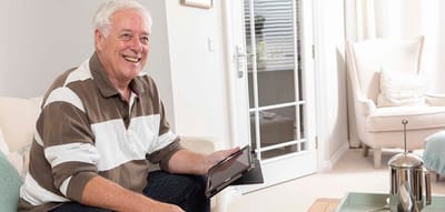 A senior man smiling while using a tablet.