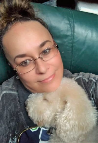 Woman cuddling a small white dog on a couch.
