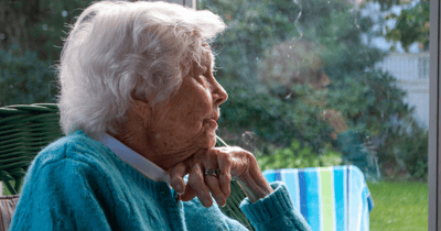 Elderly woman sitting thoughtfully outdoors.