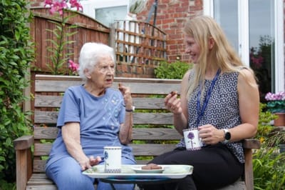 A resident and staff member enjoying snacks in a garden setting